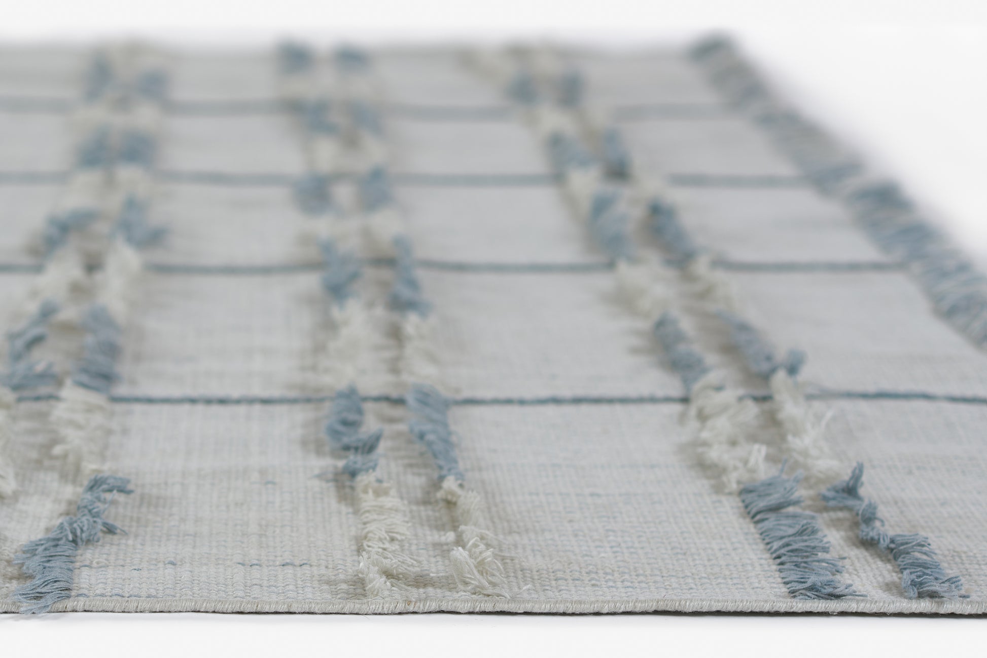 Beige woven rug with pale blue fringe stripes and a textured grid pattern, casual coastal style.