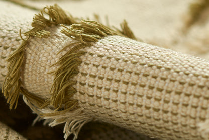 Beige woven rug with olive-green fringe tassels, close-up of textured looped weave.