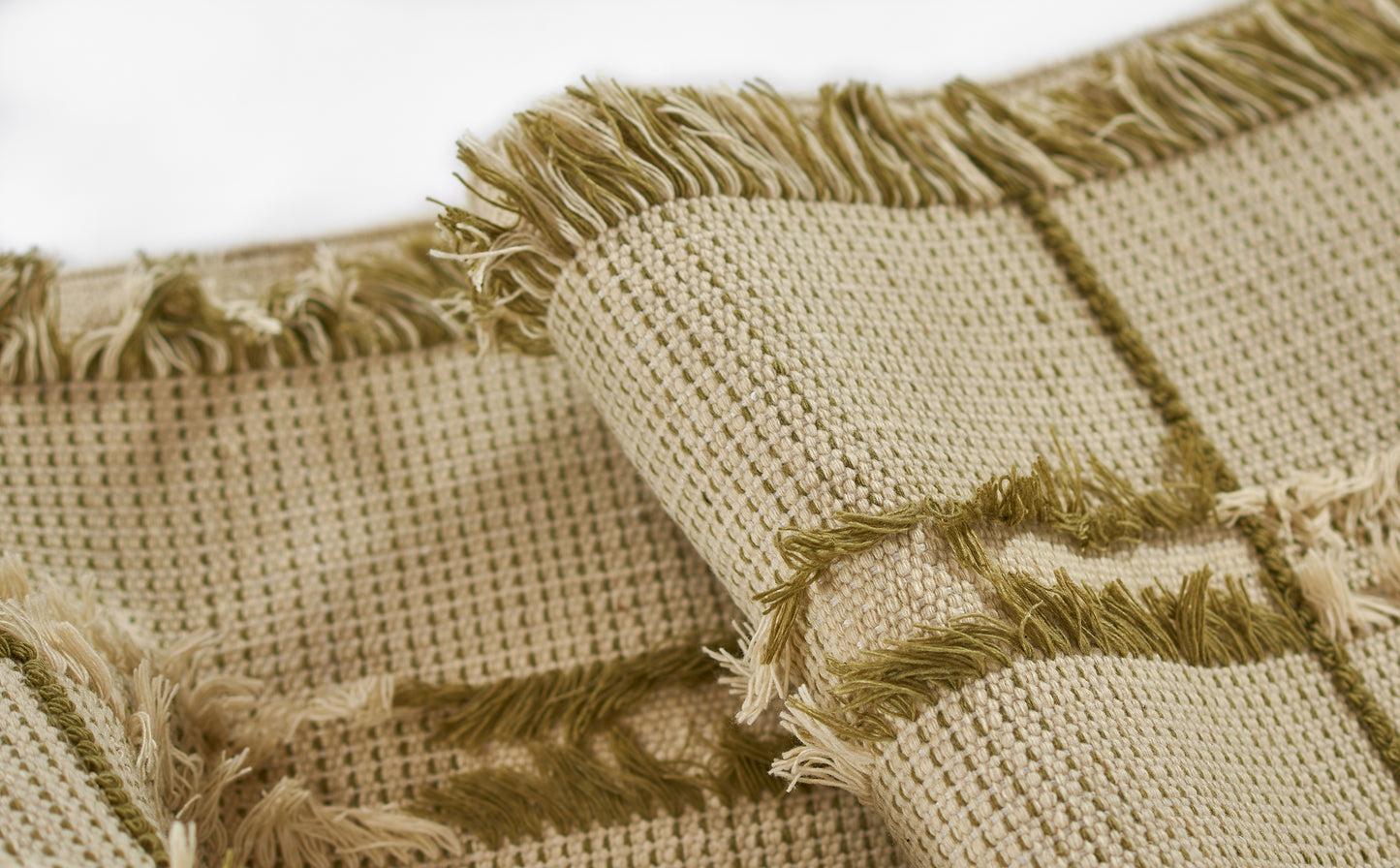 Beige woven rug with green fringe trim, textured grid weave, rustic boho style.