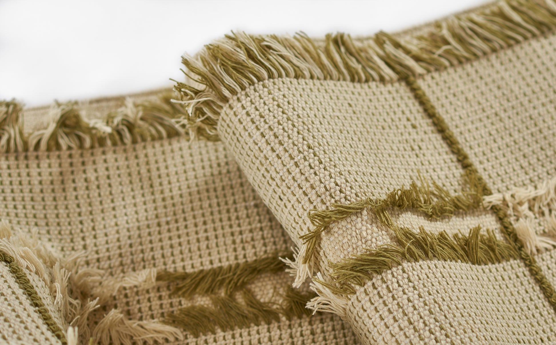 Beige woven rug with green fringe trim, textured grid weave, rustic boho style.