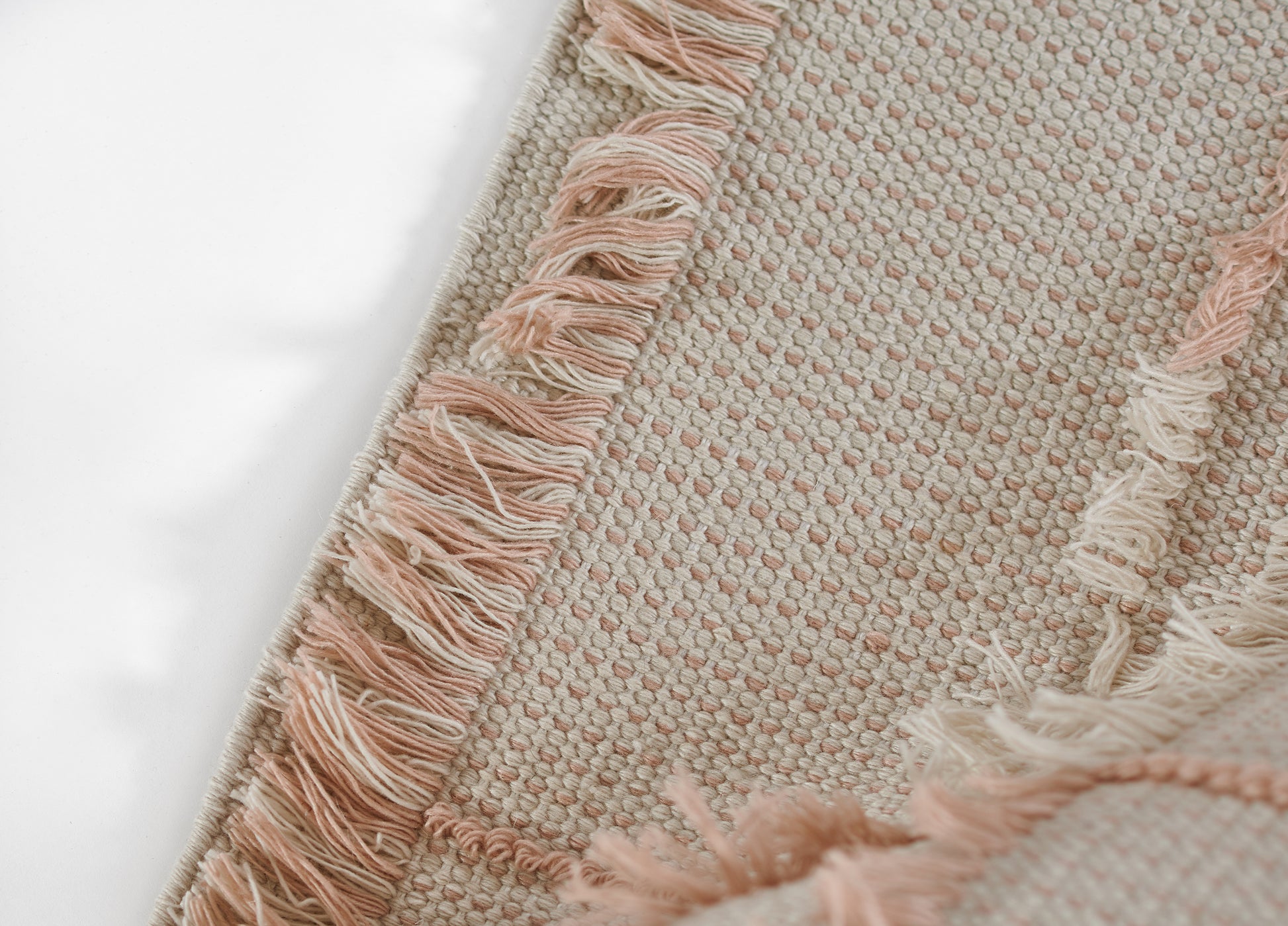 Blush pink and cream woven rug with fringe trim; textured flat-weave, boho style.