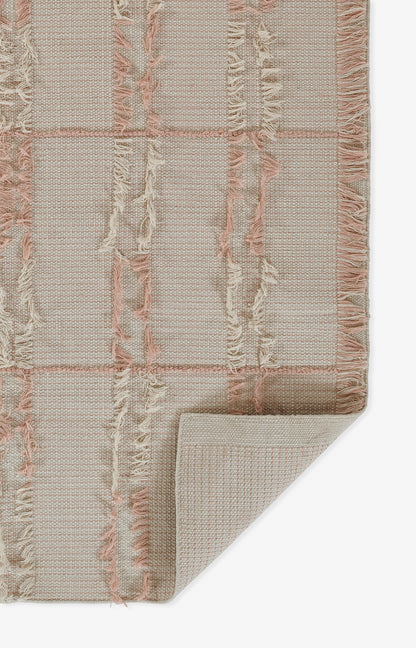 Soft pink-beige woven rug with a grid pattern and fringe tassels along the edges; folded corner shows the underside.