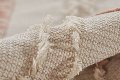 Close-up of a soft pink and ivory woven rug with fringe tassels along the edge.
