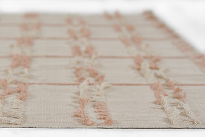 Cream flat-weave rug with blush pink geometric stripes and pink-fringed edges.