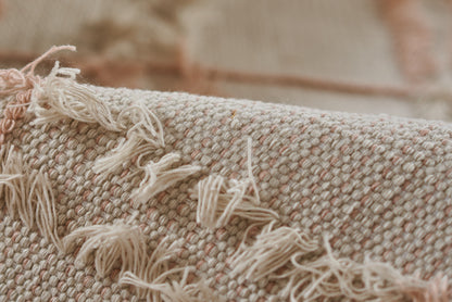 Close-up of a beige-pink woven rug with soft fringe tassels along the edge.
