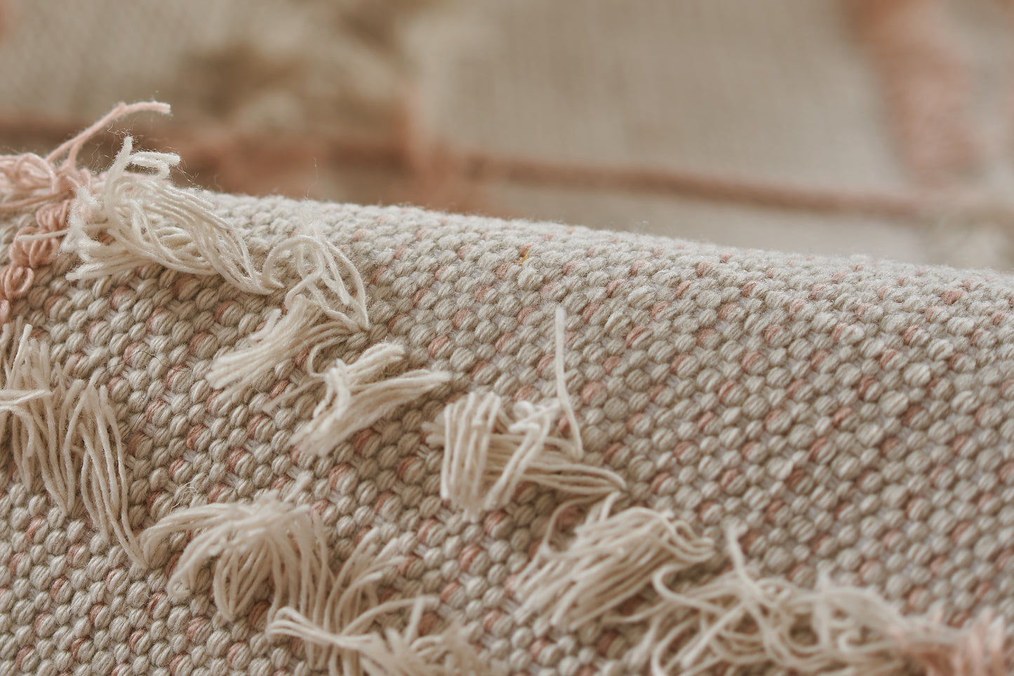 Beige-pink woven rug with fringed tassels and textured loop weave, close-up.
