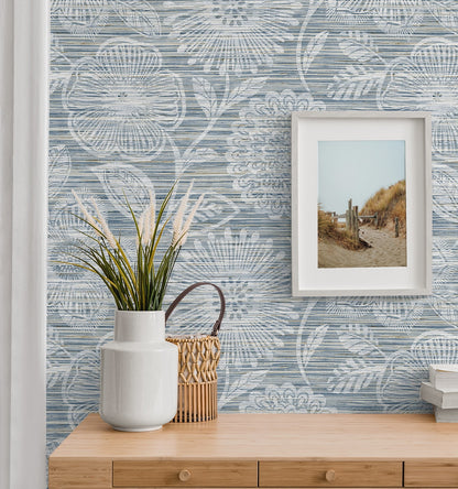 Coastal vignette with blue botanical wallpaper, light wood console, white ceramic vase, wicker basket, framed beach photo.