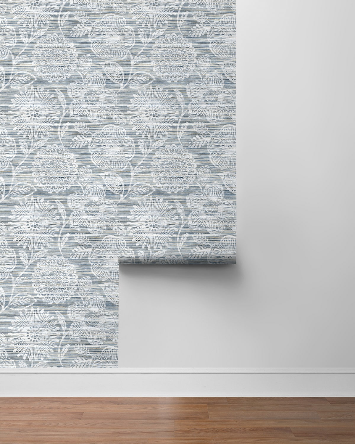 Blue-gray damask wallpaper roll with intricate medallion pattern, partially unrolled on a gray wall above a wood floor.