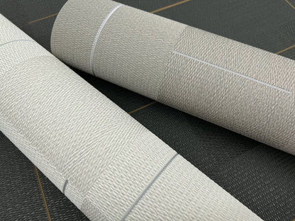Two beige textured wallpaper rolls with woven linen pattern, lying on a dark surface.
