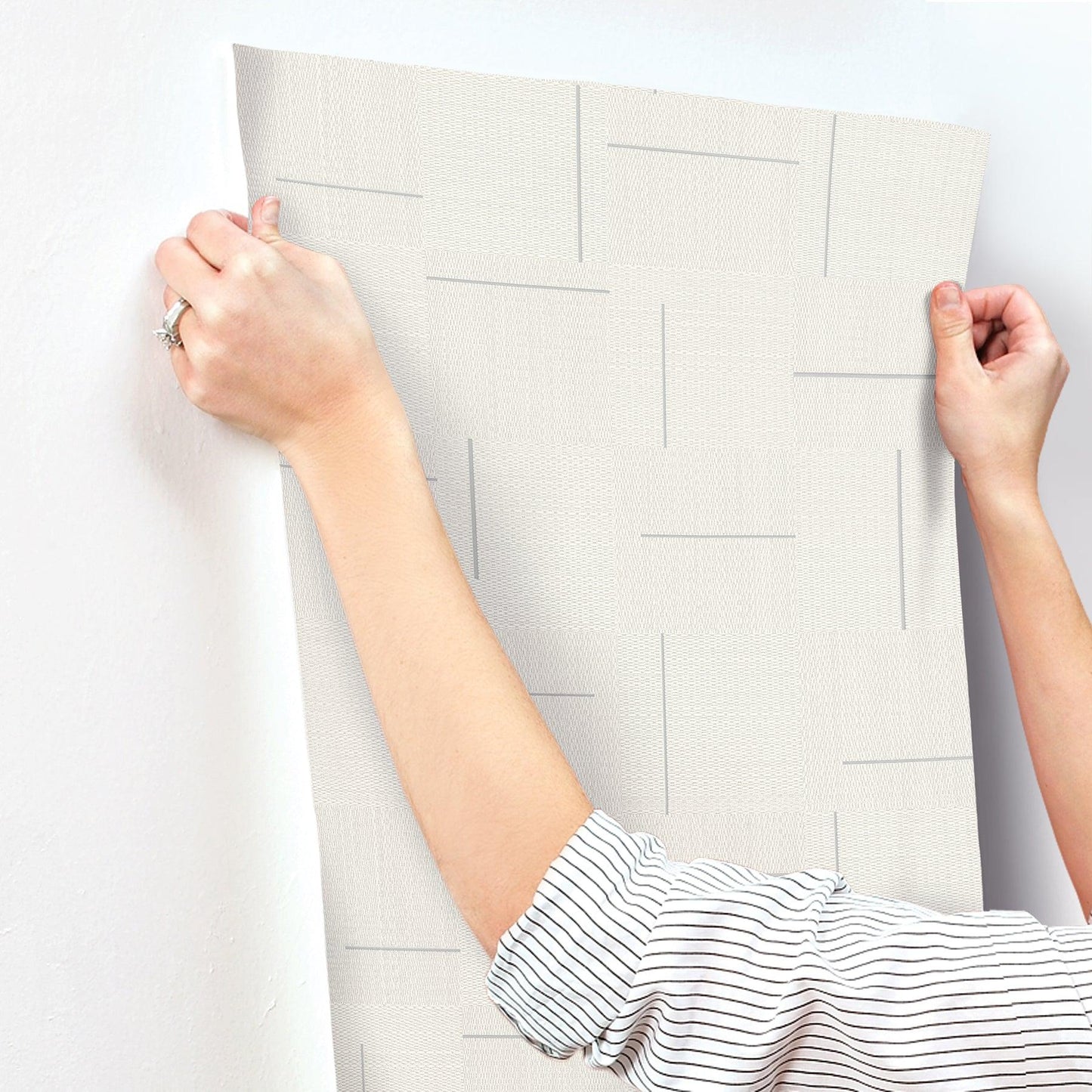 Ivory wallpaper sample with geometric rectangular line pattern, held by hands; modern home accent.