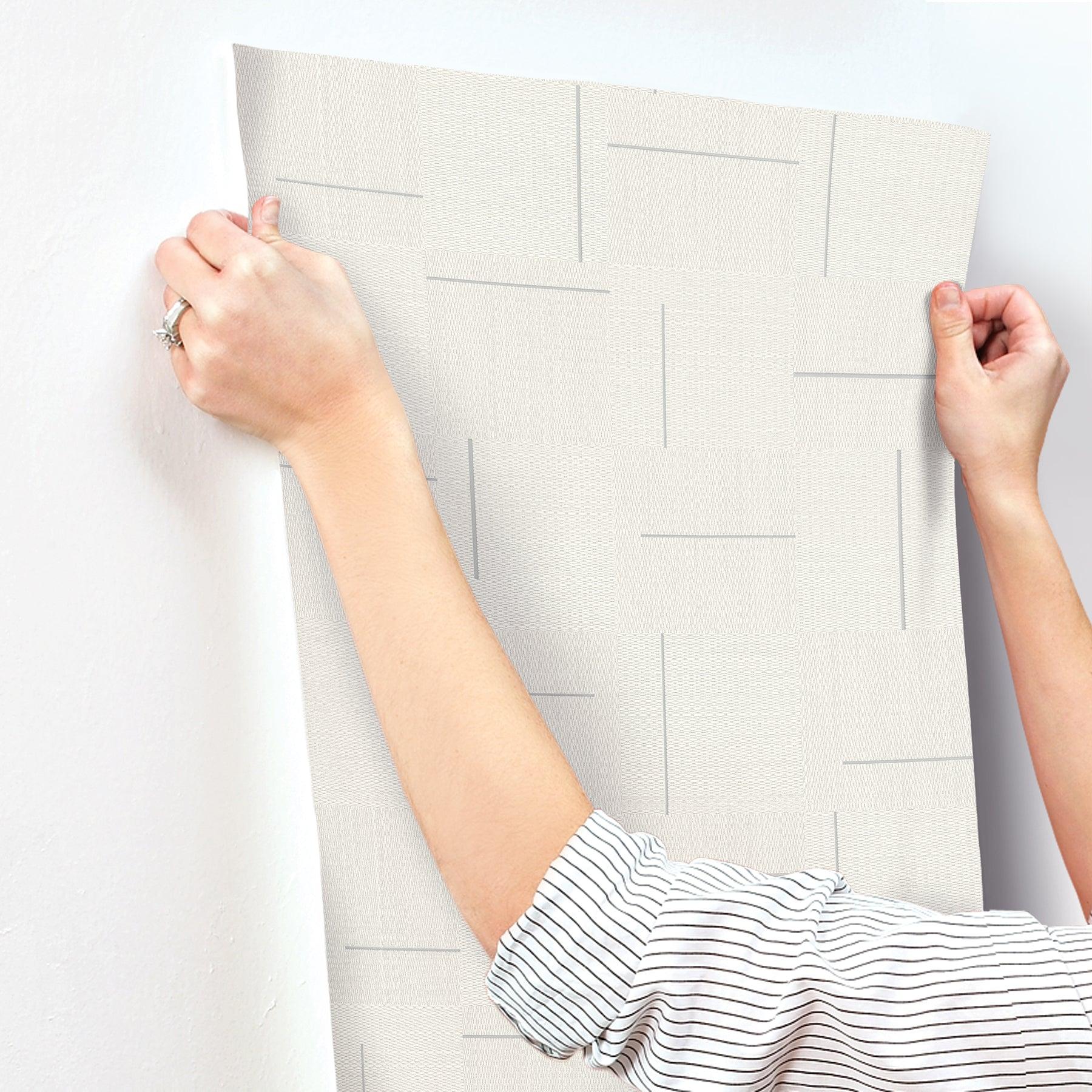 Ivory wallpaper sample with geometric rectangular line pattern, held by hands; modern home accent.