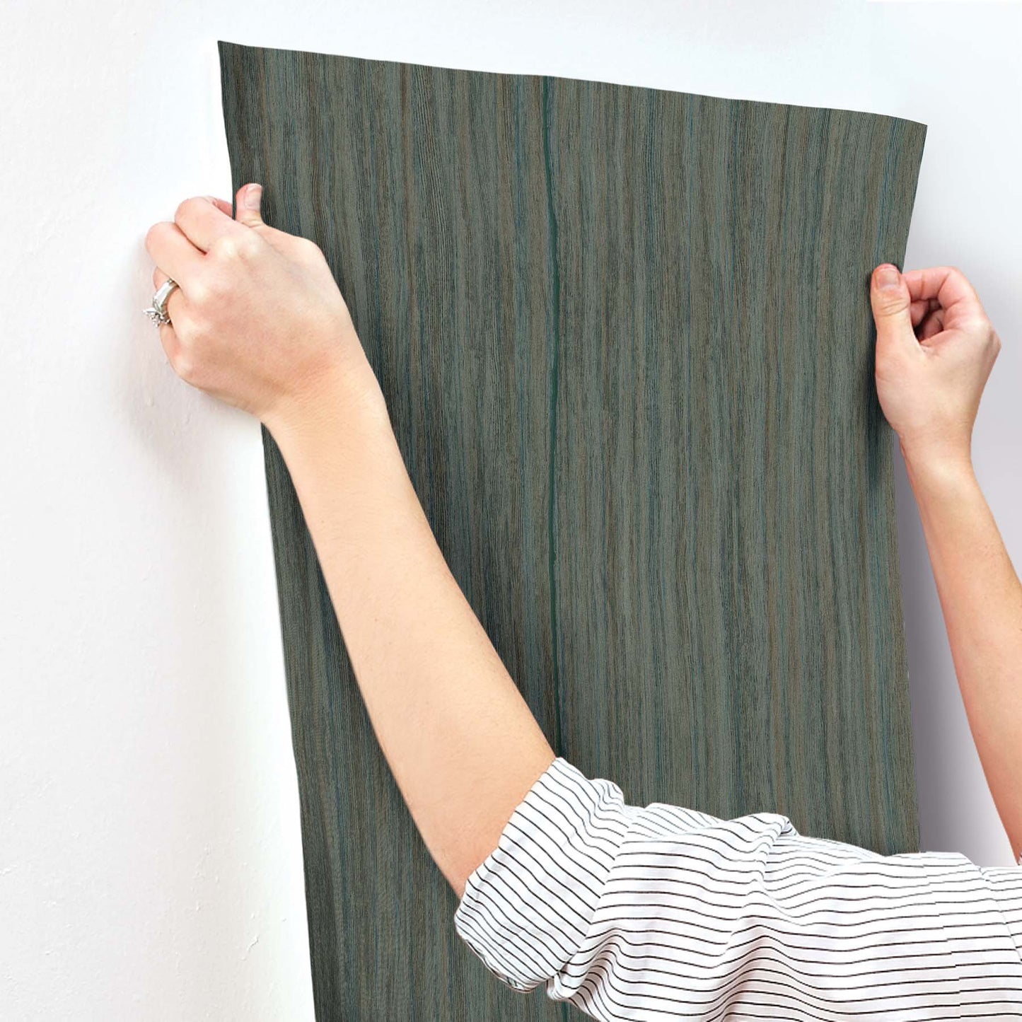 Teal striped wallpaper being smoothed onto a wall by two hands.