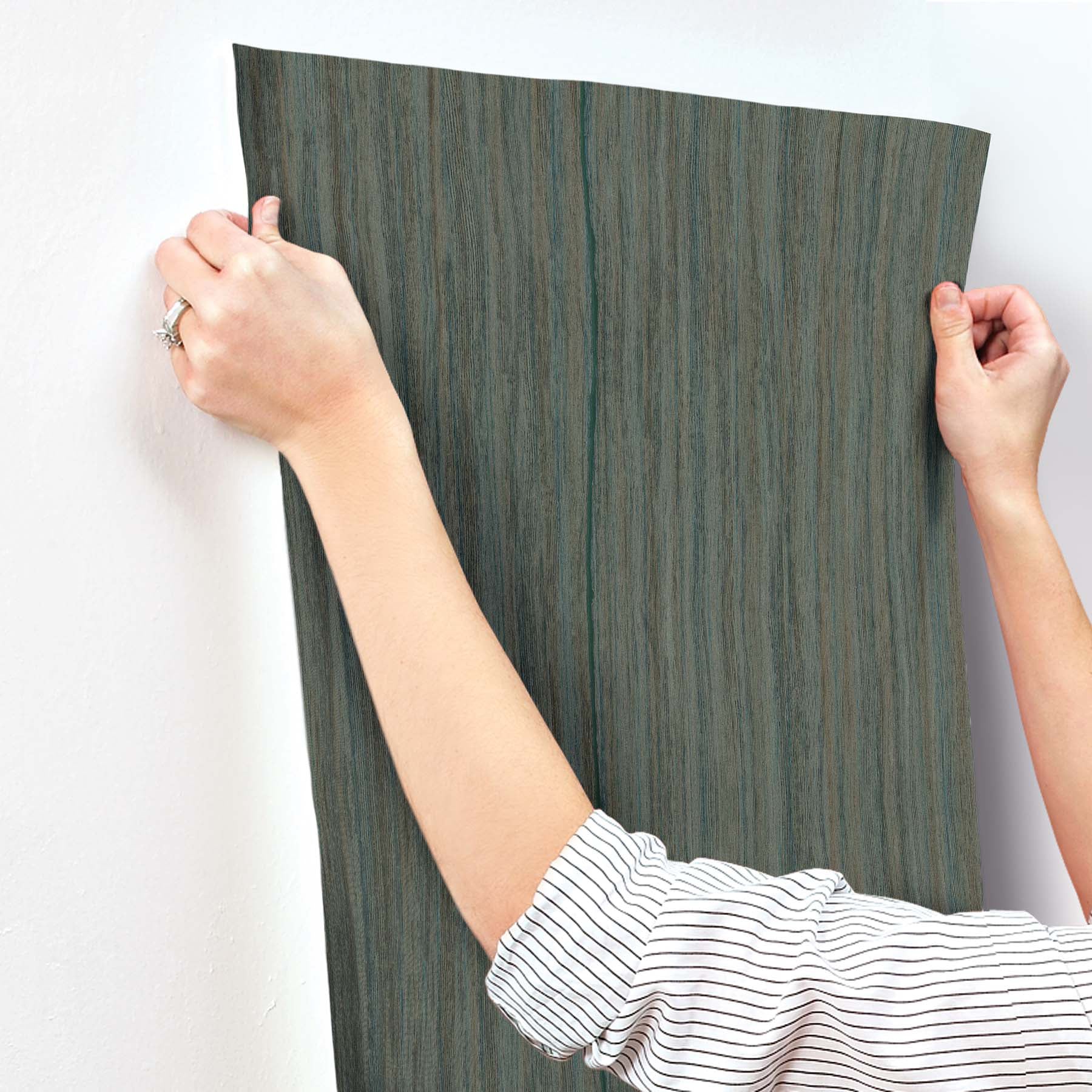 Teal striped wallpaper being smoothed onto a wall by two hands.