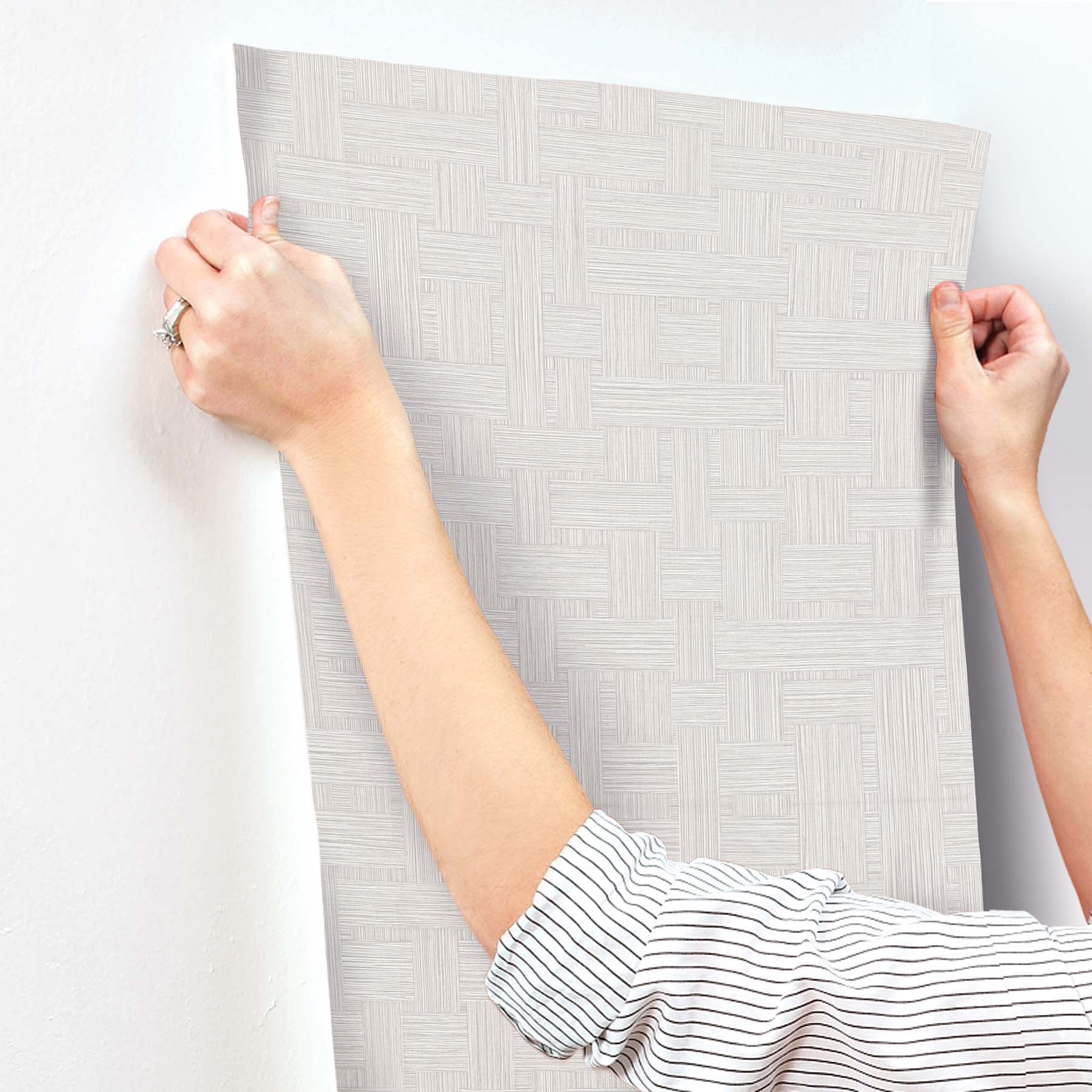 Light gray textured wallpaper with a woven basketweave pattern in a modern geometric design being applied to a wall.