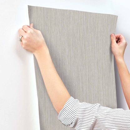 Hands apply a large grey textured wallpaper sheet to a wall; striped shirt sleeves visible.