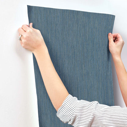 Blue denim-textured fabric panel held upright against a wall by a person in a striped shirt, wall decor sample.