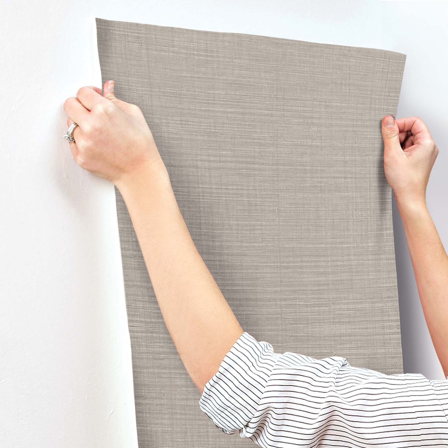 Beige linen-textured wallpaper sheet being applied to a wall; subtle crosshatched fabric look.