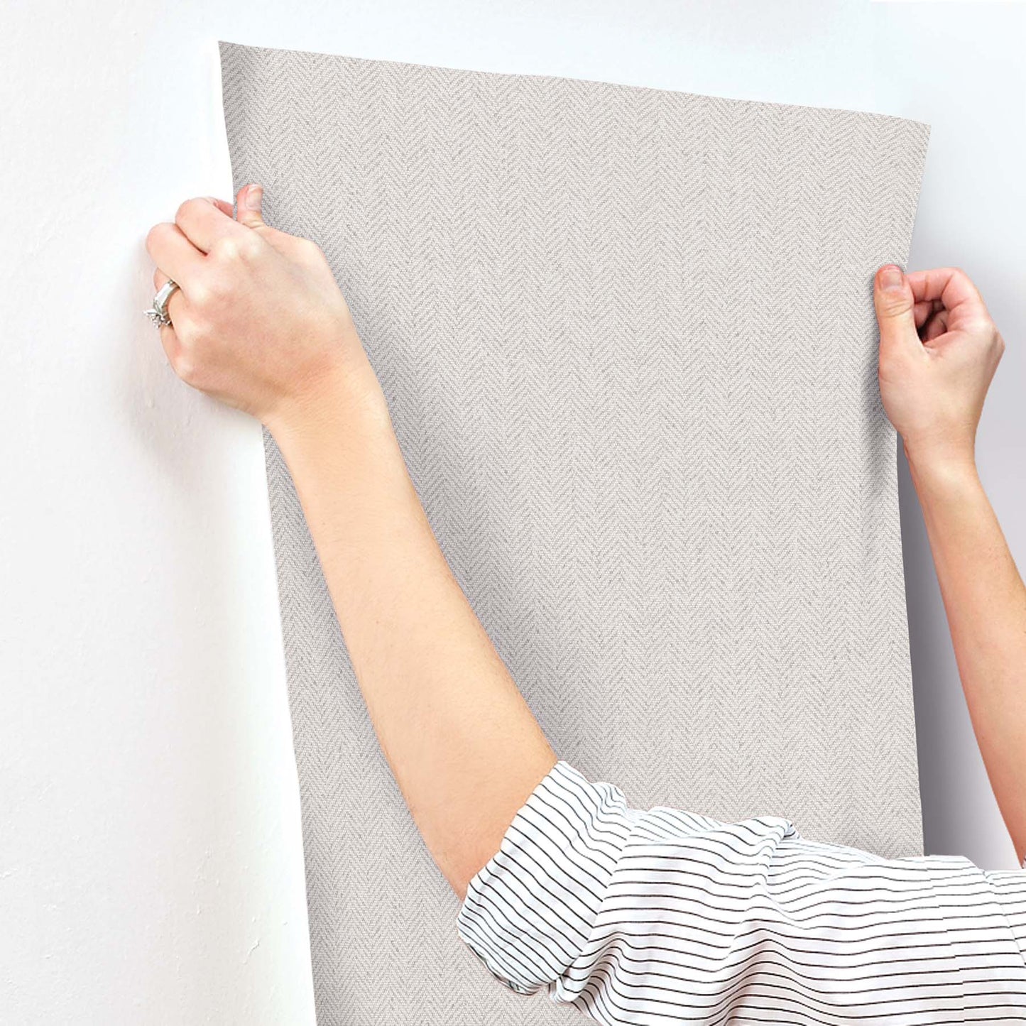 White chevron wallpaper panel being smoothed onto the wall with a handheld smoothing tool.