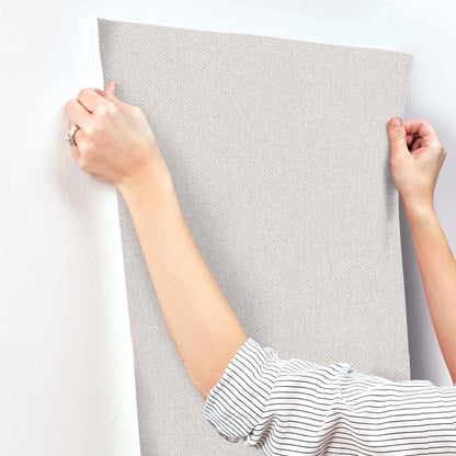 White chevron wallpaper panel being smoothed onto the wall with a handheld smoothing tool.