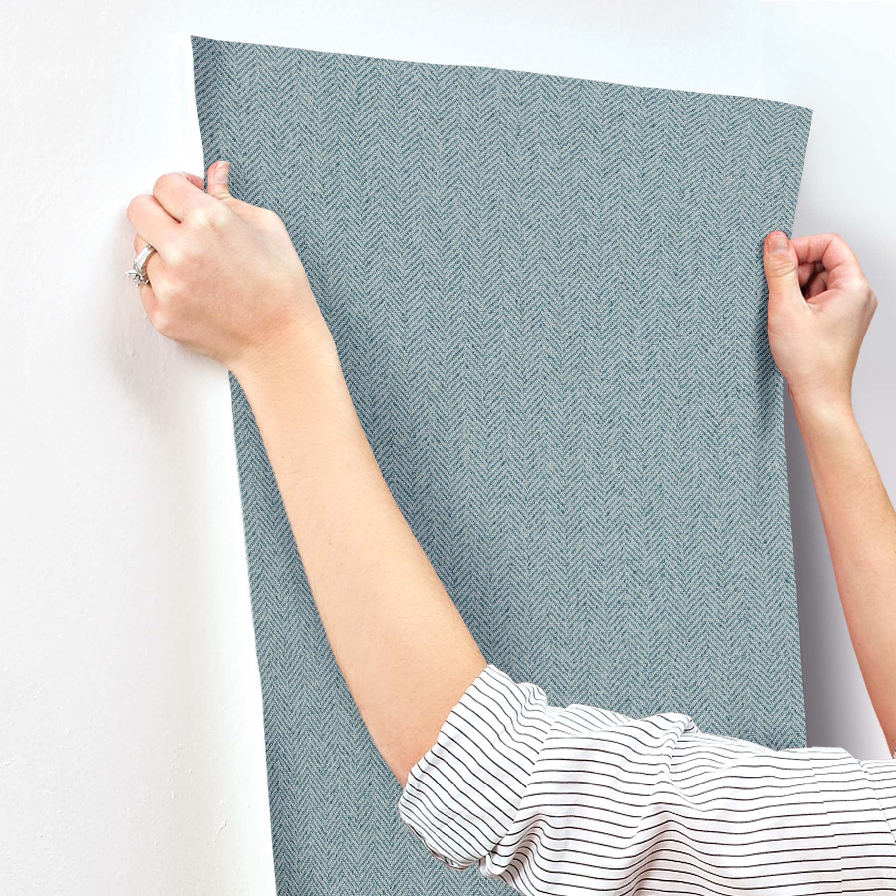 Blue chevron wallpaper being smoothed onto a wall; person holds the edge of a large sheet.