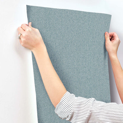 Blue chevron wallpaper being smoothed onto a wall; person holds the edge of a large sheet.