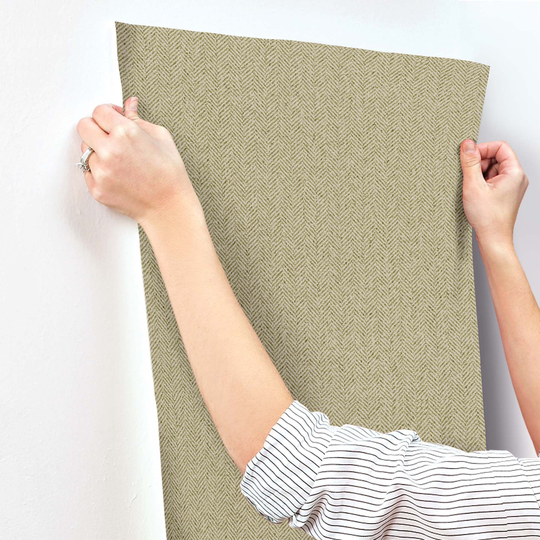 Green chevron wallpaper being smoothed onto a wall; hand in a striped shirt visible.