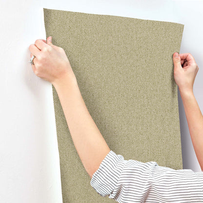Green chevron wallpaper being smoothed onto a wall; hand in a striped shirt visible.