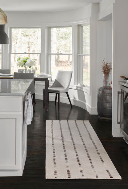 Cream runner rug with brown dotted stripes on dark wood floor beside white kitchen island and gray dining chairs