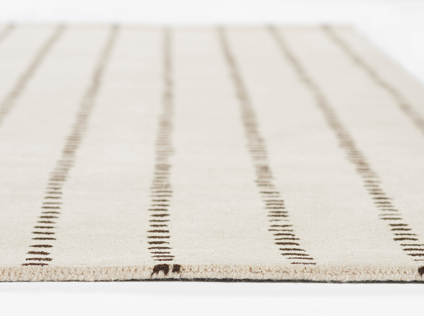 Beige flat-weave rug with dark brown vertical dashed stripes and fringe along edge.