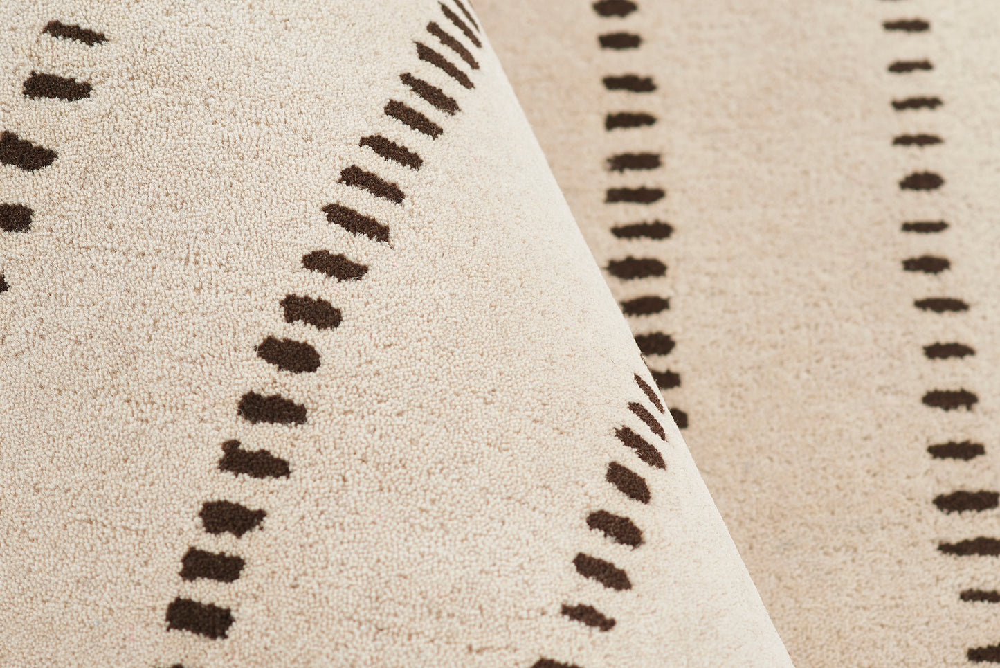 Beige plush rug with dark brown dashed line motif, soft textured pile and diagonal fold.
