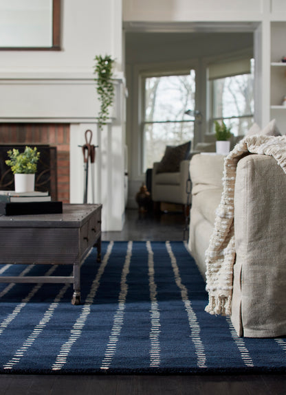 Cozy living room with navy striped rug, beige fabric sofa, fringed throw, metal coffee table, & fireplace.