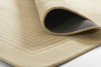 Beige textured rug with stitched rectangular border; curled corner shows dark non-slip underside.