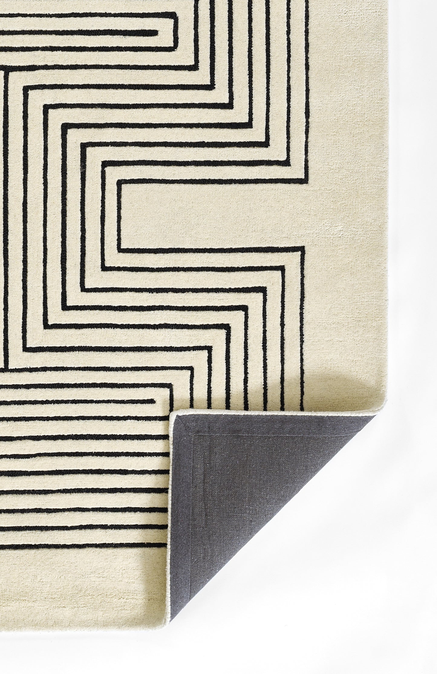 Cream rug with bold black geometric maze lines; folded corner reveals gray underside, contemporary style.