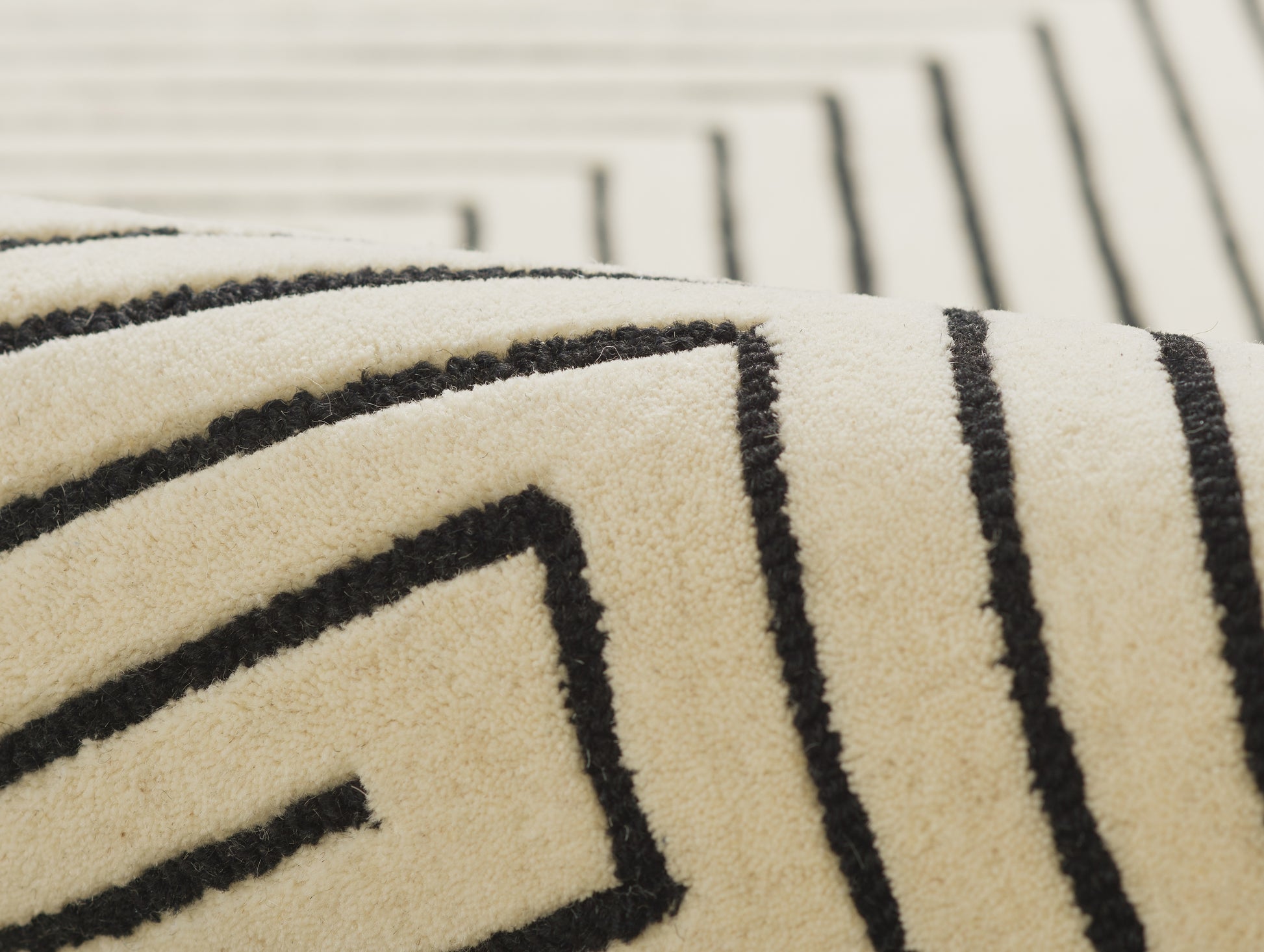 Close-up of a cream rug with bold black geometric maze/Greek-key pattern and plush pile.