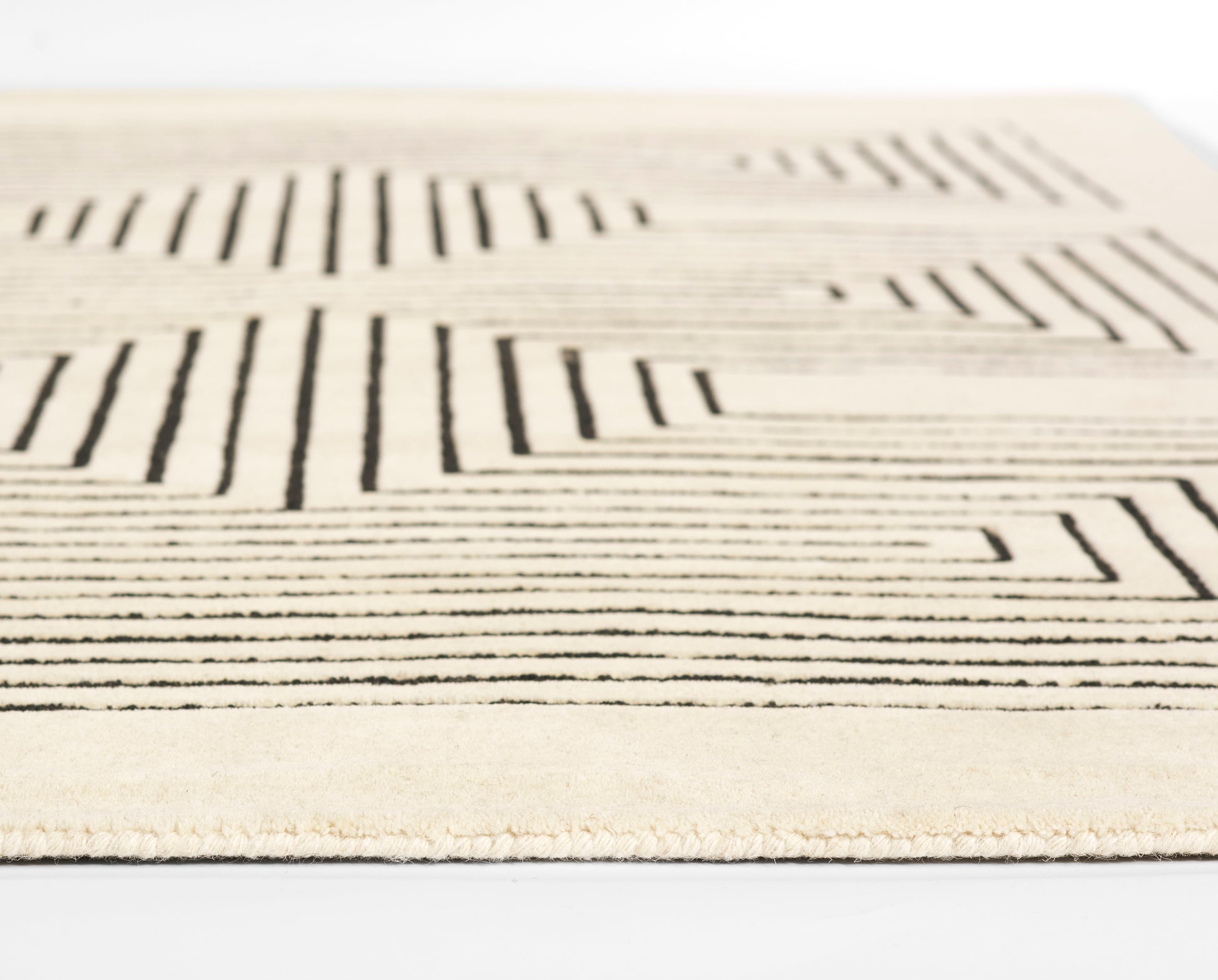 Beige rug with bold black geometric line pattern and fringed edge.
