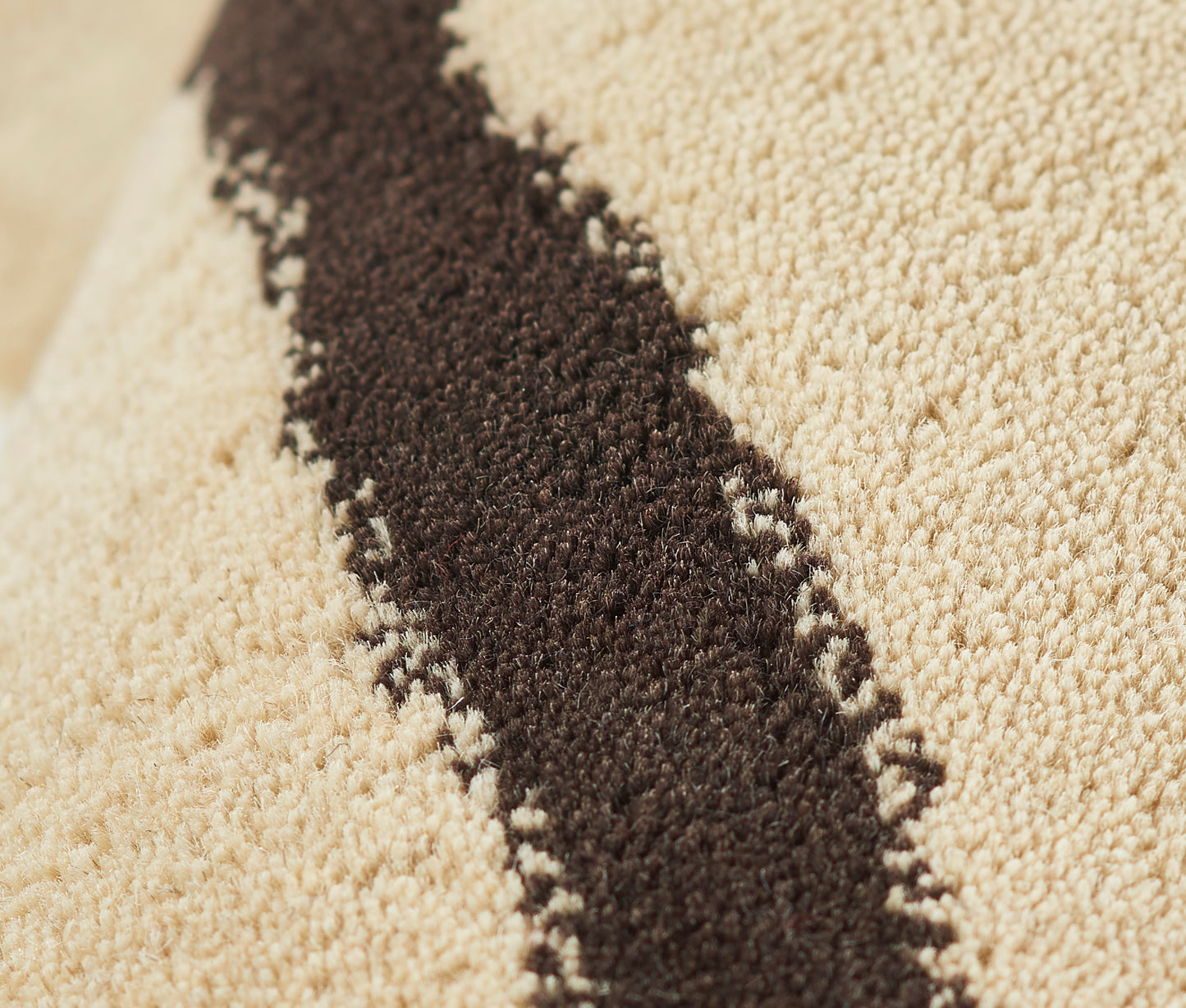 Beige plush rug with a dark brown diagonal stripe; soft loop-pile texture.