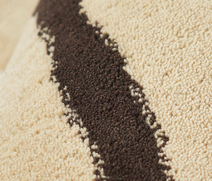 Beige plush rug with a dark brown diagonal stripe; tufted texture, modern geometric pattern.