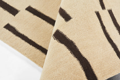 Beige tufted rug with bold dark brown abstract linear stripes; soft textured surface, geometric style.