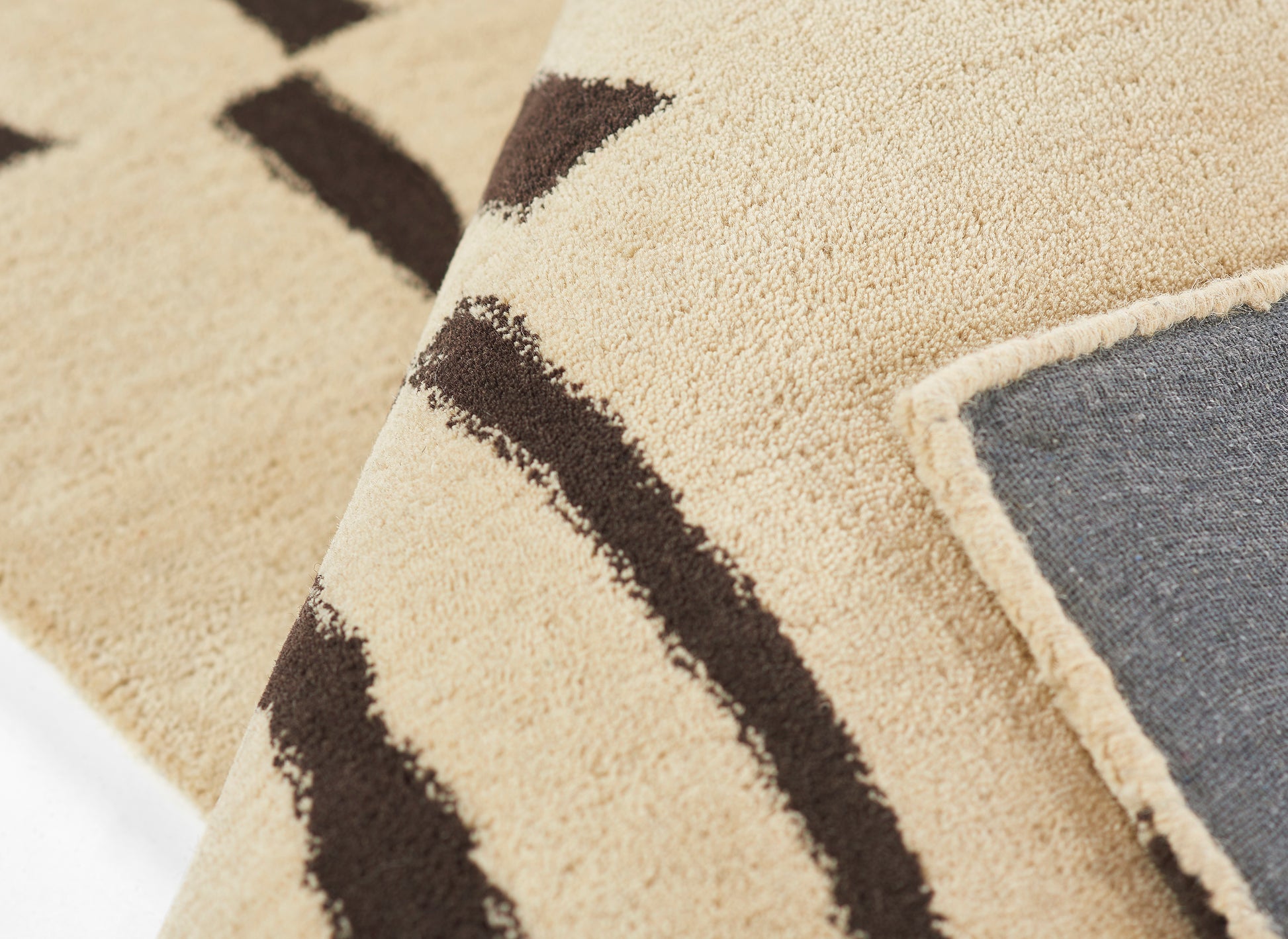 Beige tufted rug with dark brown geometric stripes; folded edge reveals blue-gray backing, cozy Boho living room decor.