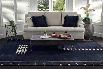 Beige sofa with navy textured pillows, dark metal coffee table, navy rug with white geometric pattern, plants.