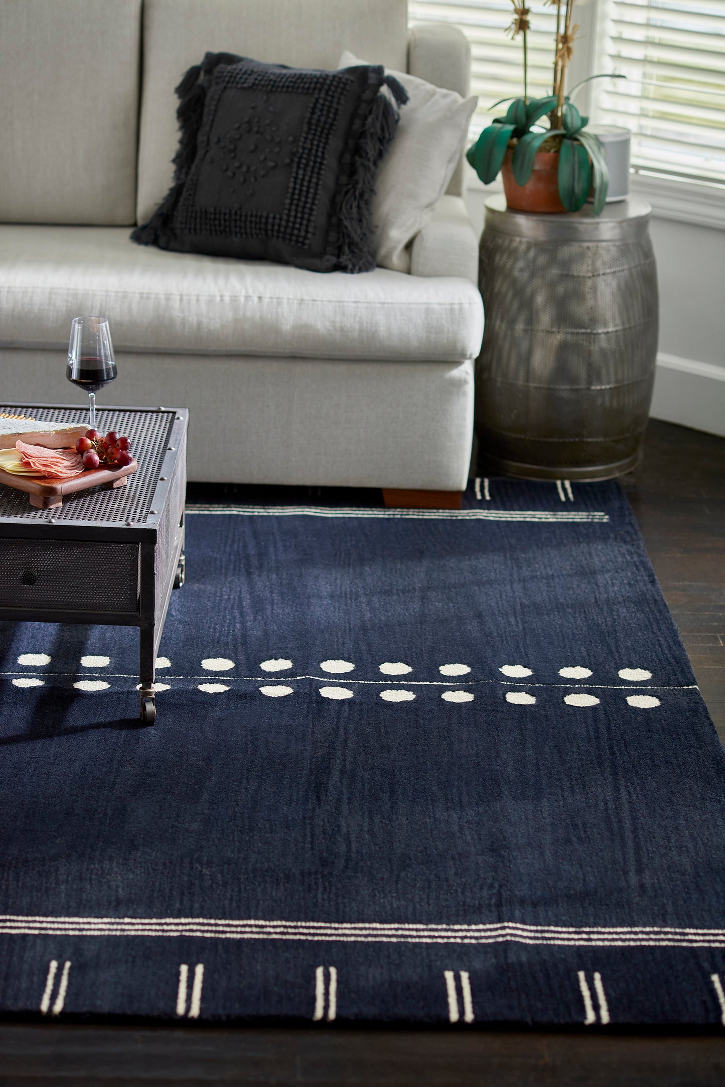 Navy area rug with white dotted lines and striped border under a black metal coffee table in a contemporary living room.