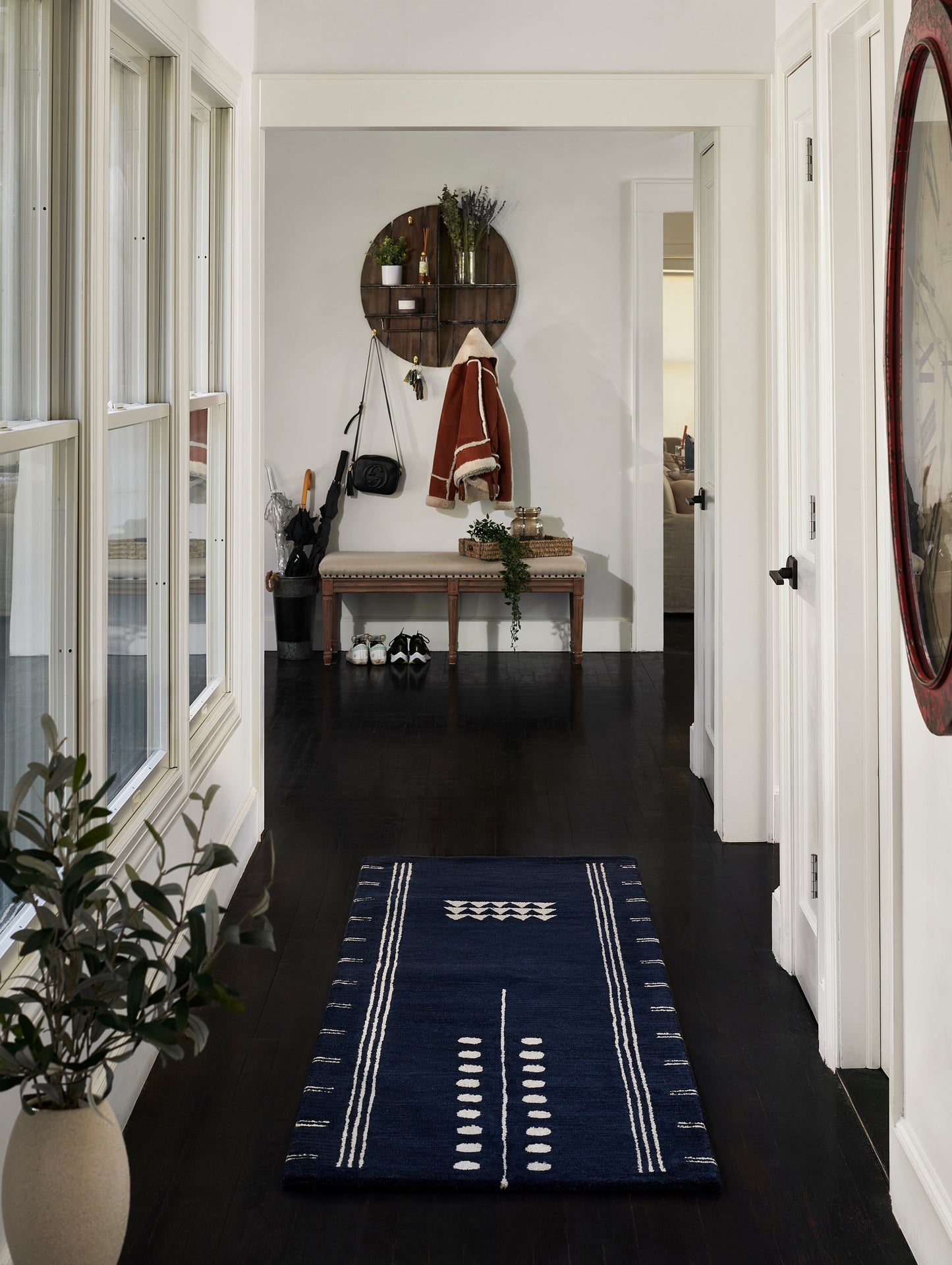 Navy hallway runner with white geometric stripes on dark wood floors; entryway with plant, circular wall shelf, coat rack.