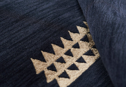 Close-up of a dark navy velvet rug with a beige triangular geometric motif.