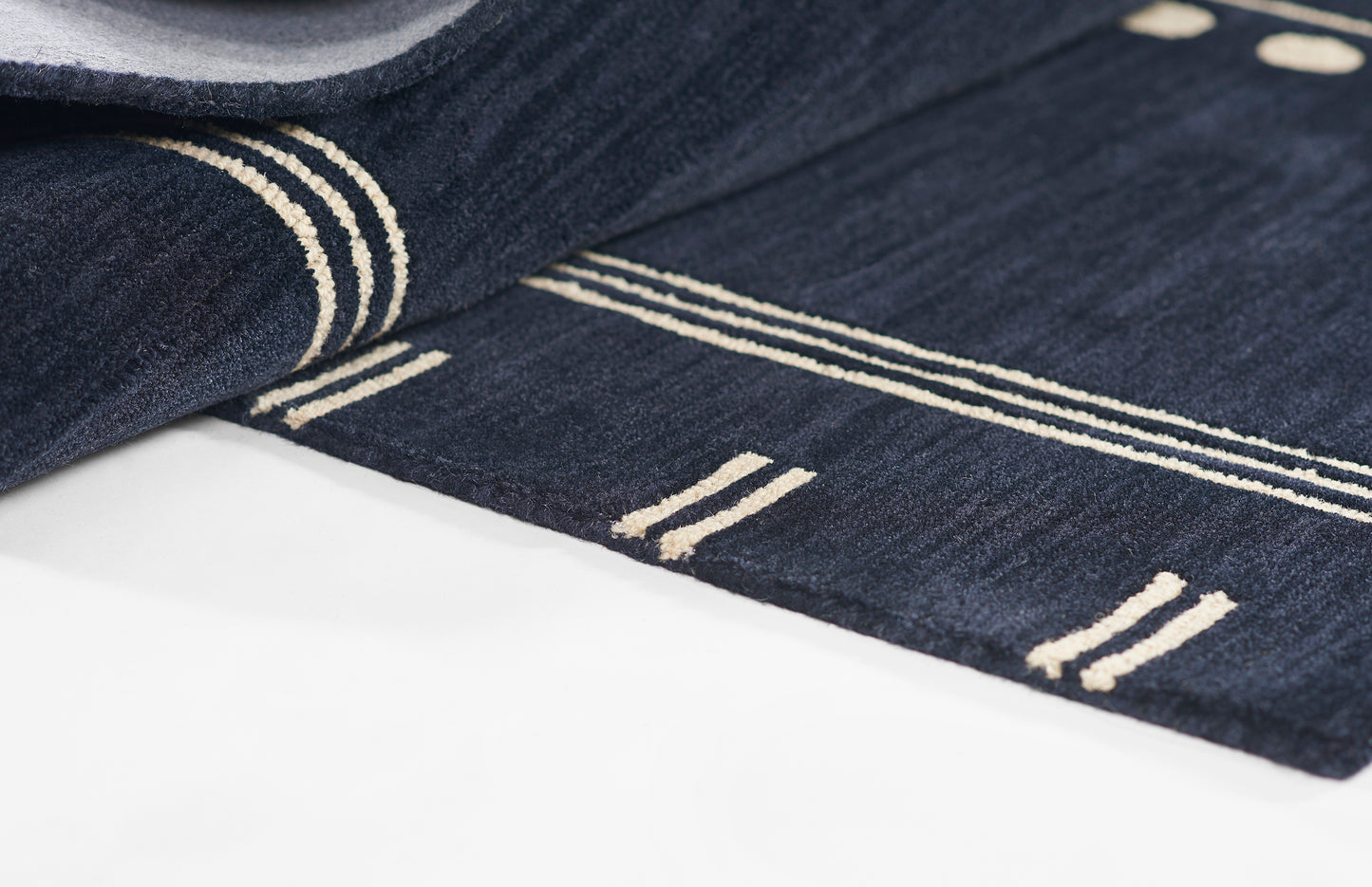 Dark navy rug with cream linear stripes, rolled edge, soft woven texture and modern geometric pattern.