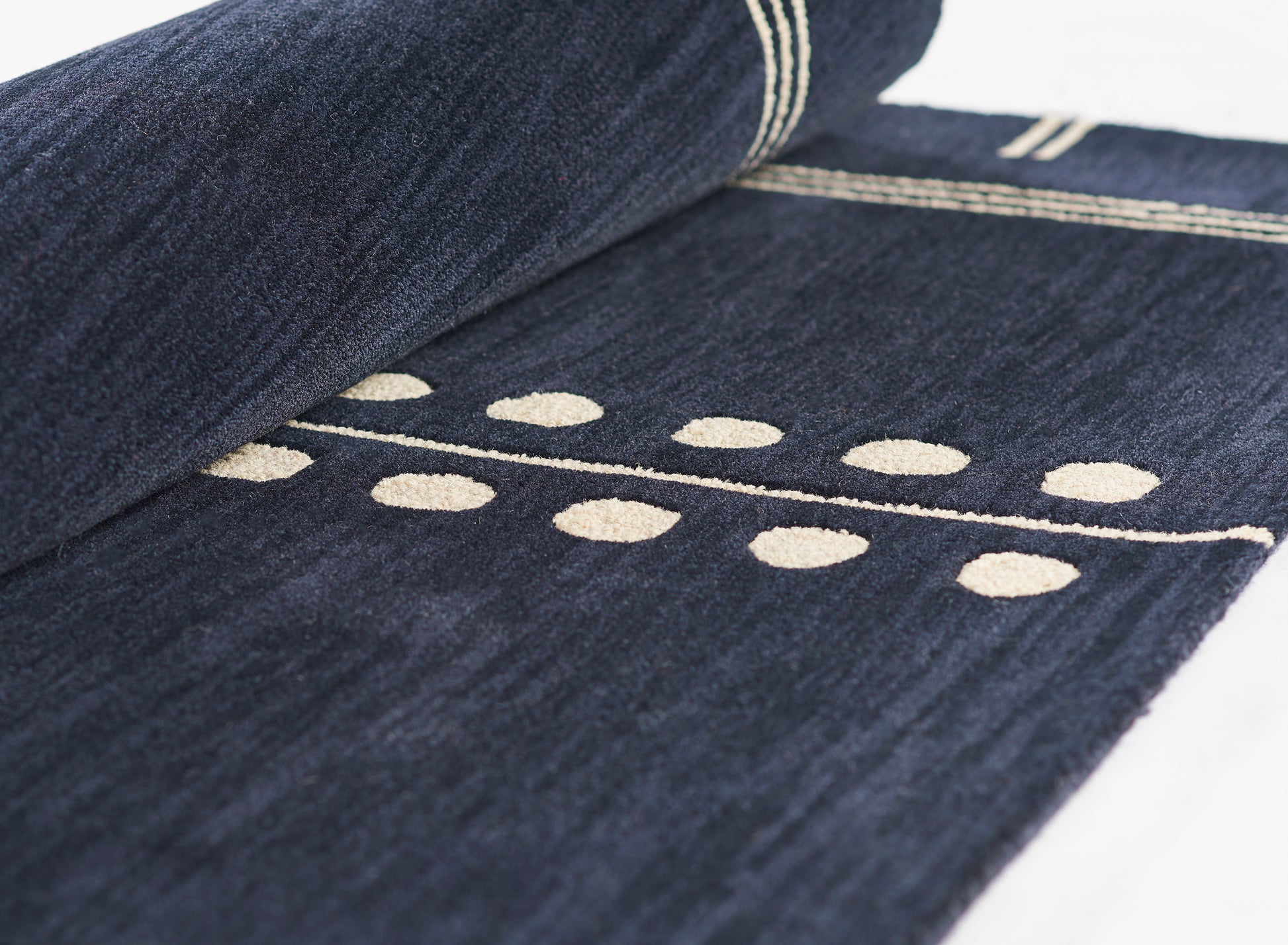 Dark indigo rug with cream circular dot pattern and white striped border; rolled presentation.