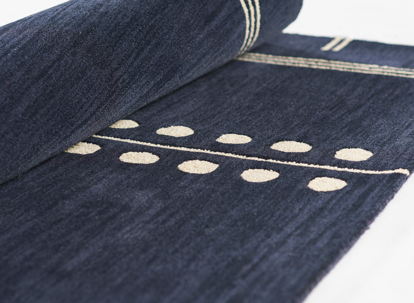 Dark indigo denim rug with cream embroidered dotted line pattern and striped border, rolled edge.