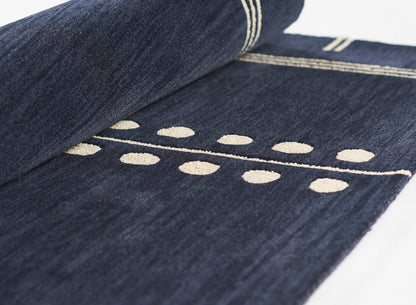 Dark indigo denim rug with cream embroidered dotted line pattern and striped border, rolled edge.