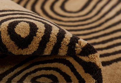 Close-up of a tan and black zebra-pattern rug with plush loop pile and swirling spiral stripes.