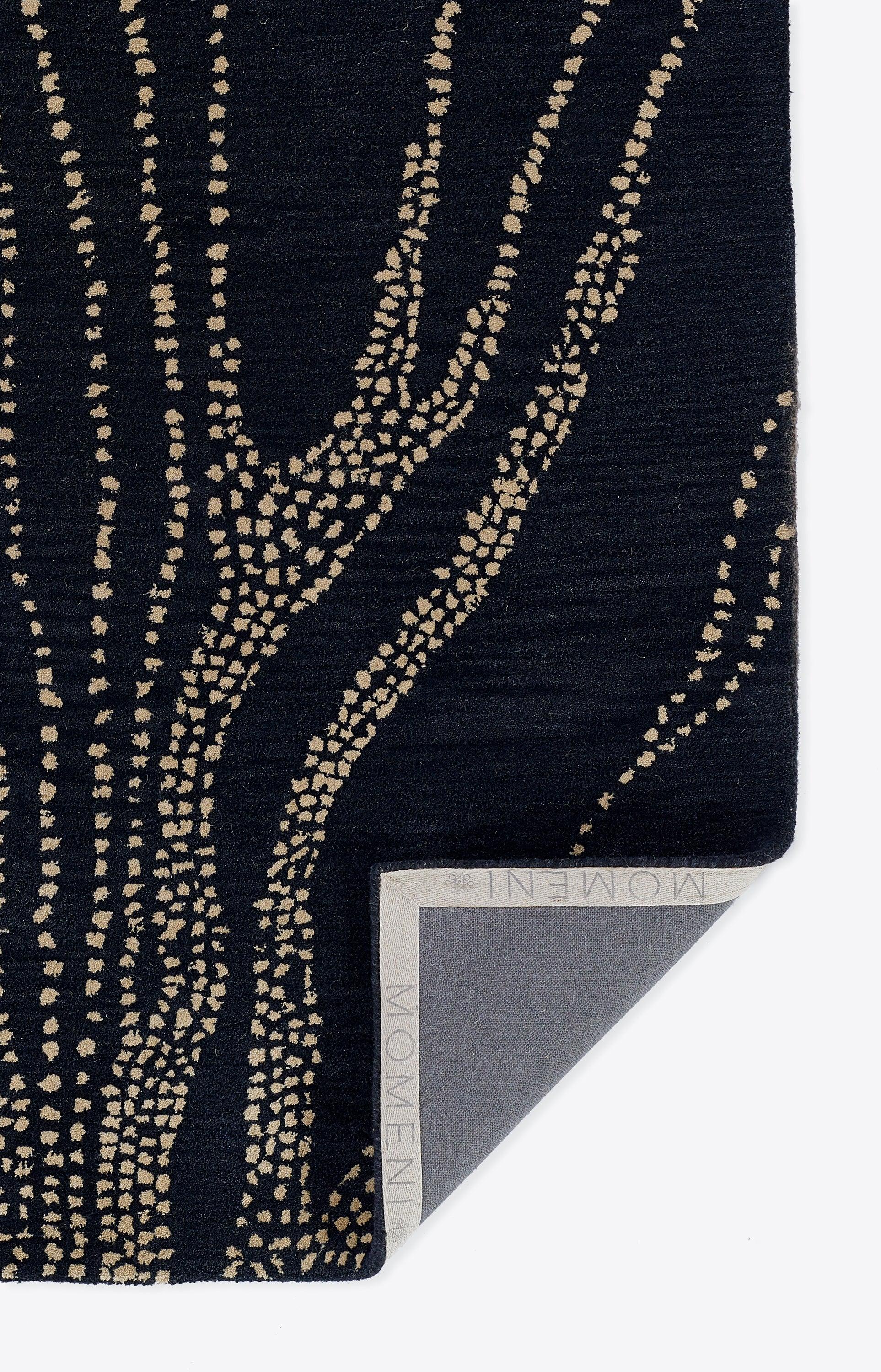 Navy rug with beige dotted branch motif on woven fabric; 5' x 8' rug; folded corner reveals label.