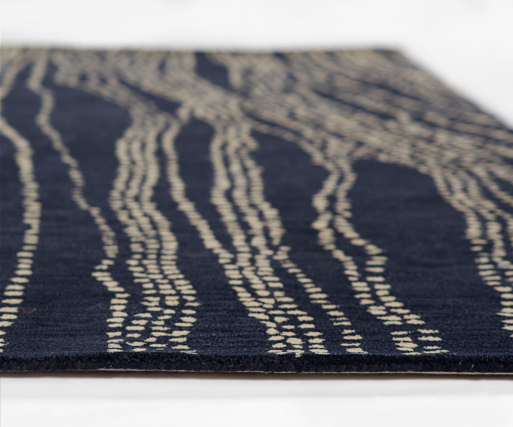 Navy rug with cream irregular wavy lines; close-up textured flat-weave edge visible.